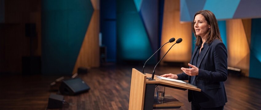 Female speaker standing at podium on conference stage. Business woman giving presentation at seminar