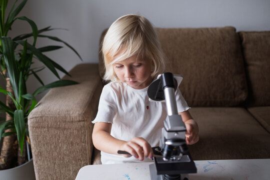 Little Girl Adjusting Microscope Slide with Tweezers at Home