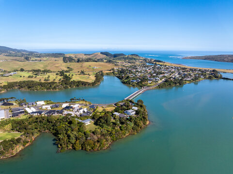 Aerial view of the coastal town of Raglan, featuring a bridge connecting residential areas across the harbour, surrounded by rolling green hills. Raglan, Waikato Region, New Zealand.