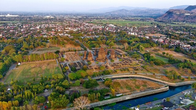 Aerial view of Prambanan Temple, an ancient Hindu temple complex surrounded by lush greenery, a river, and the town of Kecamatan Prambanan, Daerah Istimewa Yogya, Indonesia.