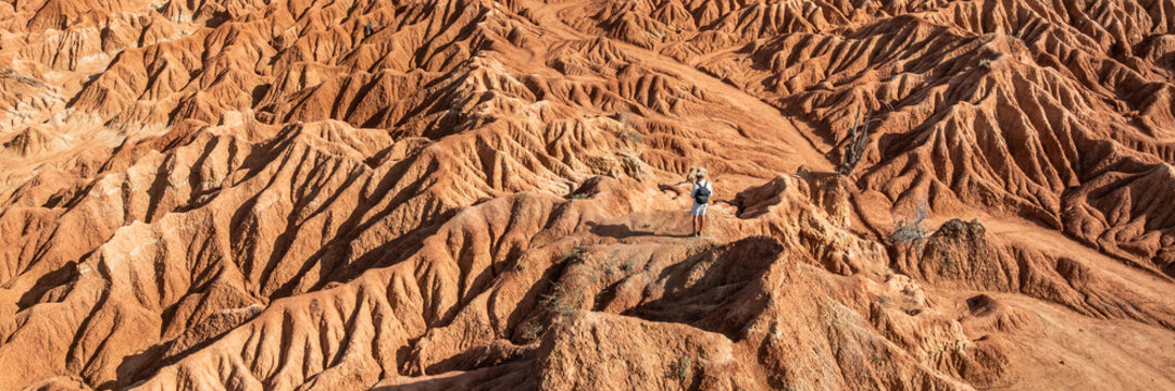 Aerial view of the Tatacoa Desert red desert with eroded clay formations and a person standing on a ridge in Villavieja, Huila, Colombia.