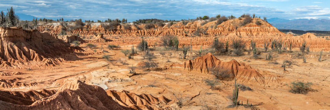 Aerial view of the Tatacoa Desert red desert, featuring eroded clay formations, cacti, and arid landscape under a blue sky in Villavieja, Huila, Colombia.