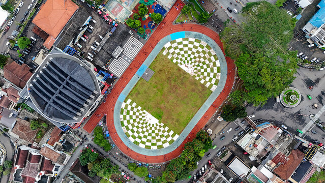 Aerial view of Taman Kota Lapang Merdeka Sukabumi featuring a unique checkered field pattern surrounded by a red running track and urban infrastructure, Sukabumi, West Java, Indonesia.
