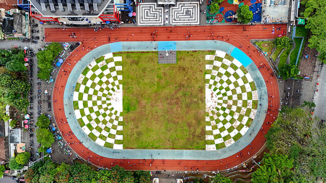 Aerial view of Taman Kota Lapang Merdeka Sukabumi featuring a distinctive checkerboard patterned field surrounded by a red running track with people walking in Sukabumi, West Java, Indonesia.
