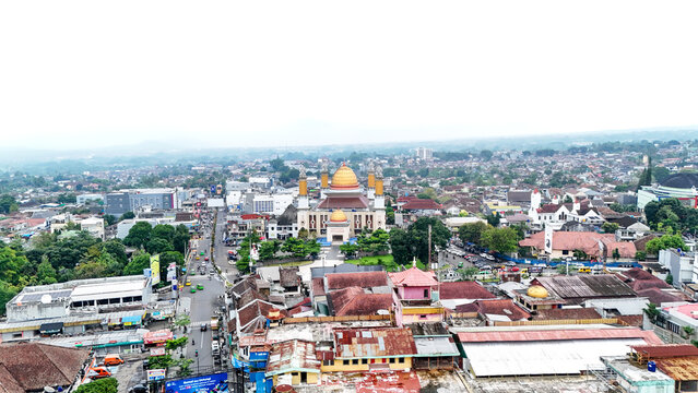 Aerial view of Masjid Agung Kota Sukabumi surrounded by dense urban rooftops, lush trees, and city streets in Sukabumi, West Java, Indonesia.