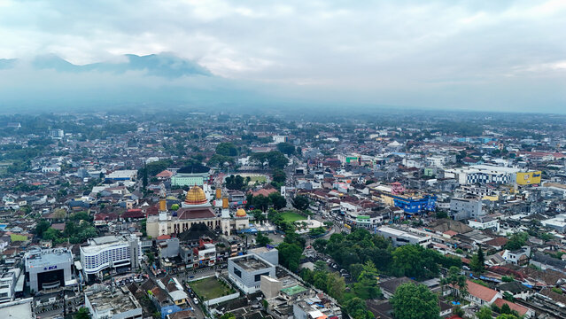 Aerial view of Masjid Agung Kota Sukabumi with its golden dome surrounded by the dense urban landscape, rooftops, and lush greenery in Sukabumi, West Java, Indonesia.