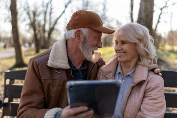 Elderly man and woman exploring a digital tablet together in a peaceful park, illustrating digital literacy, lifelong learning and technology adoption among seniors © lordn