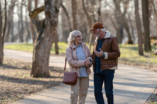 Cheerful senior couple enjoying a walk together in a sunlit park, holding hands and talking while maintaining an active, healthy and socially connected retirement lifestyle