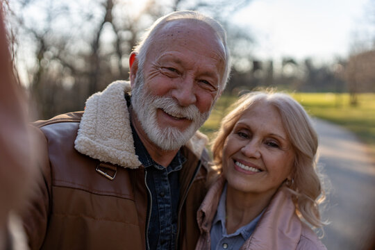 Smiling senior couple taking a close-up selfie outdoors, illustrating smartphone photography, digital confidence and modern technology use among older adults.