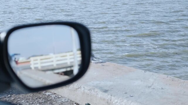 View from the car Mirror: A serene seascape unfolds as the side mirror of a car captures a bridge and the vast ocean, inviting a sense of journey and reflection.