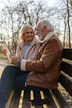 Elderly man and woman exploring a digital tablet together in a peaceful park, illustrating digital literacy, lifelong learning and technology adoption among seniors