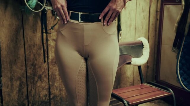 Closeup of female rider adjusting tall black boots inside stable. Riding footwear, equestrian clothing concept.