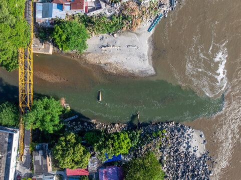 Aerial view of the confluence of the Guali and Magdalena rivers in Honda, showing the contrasting water colors, a yellow bridge, and rocky riverbanks, Honda, Tolima, Colombia.