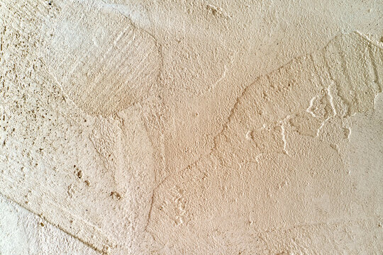Beige plaster wall texture close-up with rough surface, shallow cracks, and faint stains, ideal background material for interior design and construction concepts