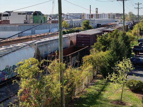 Aerial view of a long freight train moving through an industrial area with urban buildings, railway tracks, and green trees in Cincinnati, Ohio, United States.