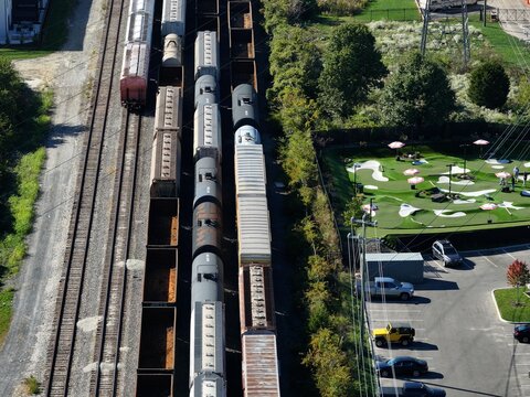 Aerial view of freight train cars on parallel tracks adjacent to a mini golf course and a parking lot in Cincinnati, Ohio, United States.