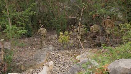 Fototapeta premium A squad of elite soldiers in full tactical gear carefully advances through a rugged jungle environment on a covert reconnaissance mission, displaying teamwork and vigilance.