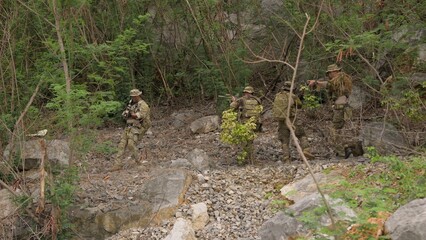 Fototapeta premium A squad of elite soldiers in full tactical gear carefully advances through a rugged jungle environment on a covert reconnaissance mission, displaying teamwork and vigilance.