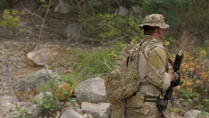 Fototapeta premium A soldier in full combat gear patrols through a rugged, rocky wilderness on a reconnaissance mission, showcasing tactical readiness and strategic surveillance.