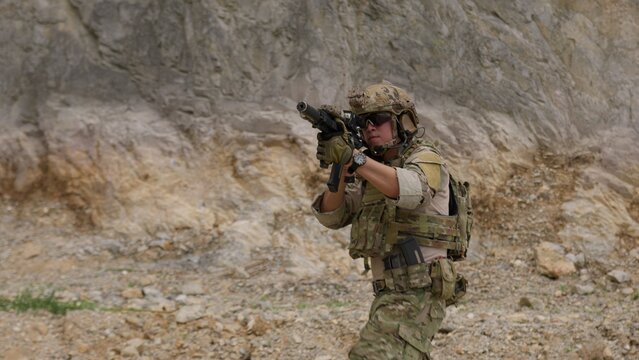A special forces operator in full combat gear advances cautiously through a rocky, hostile environment while aiming his assault rifle on a tactical security patrol.