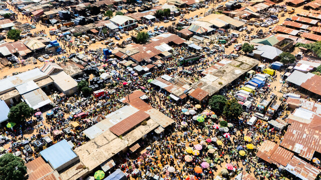 Aerial view of the bustling Building Materials Market with dense rows of stalls, corrugated metal roofs, and crowds of people navigating the busy marketplace in Jos, Plateau, Nigeria.