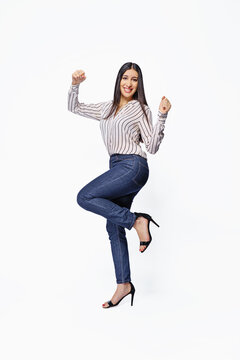 An enthusiastic woman celebrates with her arms raised against a white background. Full-body photo.