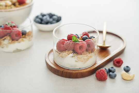 Yogurt dessert with granola and fresh raspberries and blueberries in a glass, served with a spoon