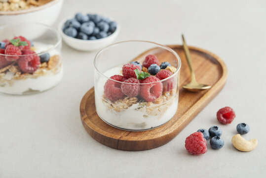 Yogurt dessert with granola and fresh raspberries and blueberries in a glass, served with a spoon