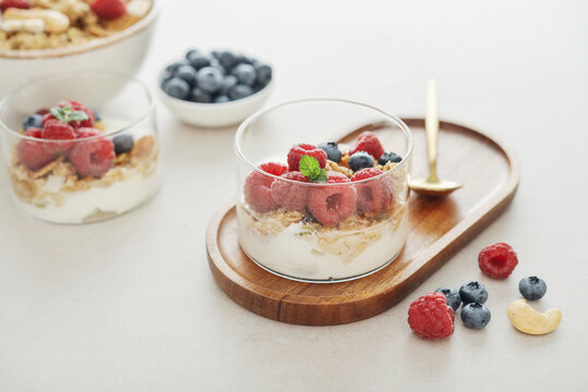 Yogurt dessert with granola and fresh raspberries and blueberries in a glass, served with a spoon