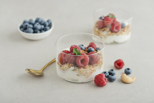 Yogurt dessert with granola and fresh raspberries and blueberries in a glass, served with a spoon