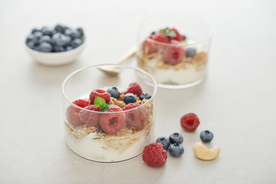 Yogurt dessert with granola and fresh raspberries and blueberries in a glass, served with a spoon