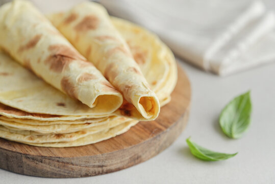 Stack of lavash or chapati flatbreads on a wooden cutting board, with a jar of flour, fresh basil