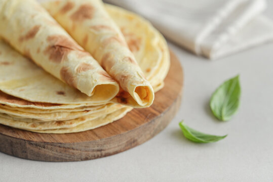 Stack of lavash or chapati flatbreads on a wooden cutting board, with a jar of flour, fresh basil