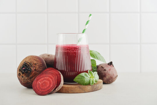 Beetroot juice in a glass with a striped paper straw, served with raw beetroot and fresh basil