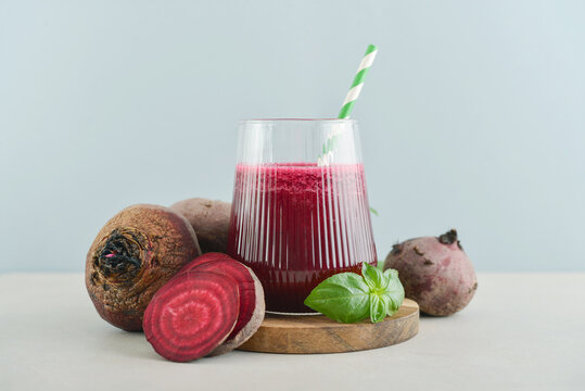Beetroot juice in a glass with a striped paper straw, served with raw beetroot and fresh basil