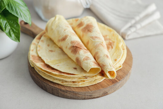 Stack of lavash or chapati flatbreads on a wooden cutting board, with a jar of flour, fresh basil