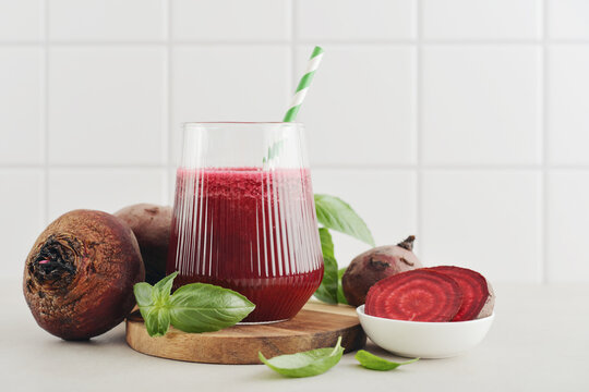 Beetroot juice in a glass with a striped paper straw, served with raw beetroot and fresh basil