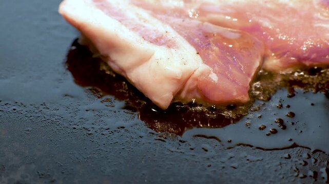 鉄板の上でバターと油に包まれて焼かれる豚ロースステーキ、シズル感のあるクローズアップ