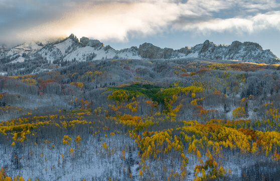 Aerial view of the snow-dusted Ruby Peak rising above a vibrant forest of golden autumn aspen trees in Kebler Pass, Crested Butte, Colorado, United States.