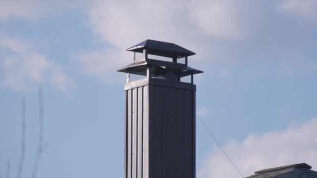 Tall metal chimney stands against blue sky with clouds in background during day