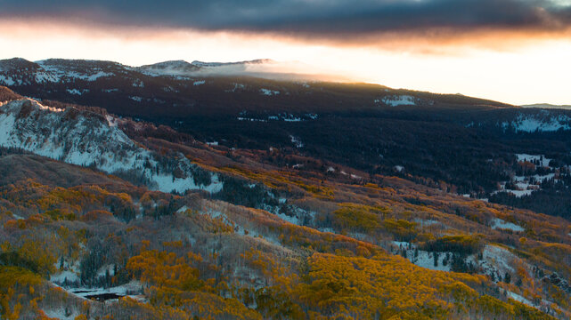 Aerial view of Kebler Pass at sunrise, featuring golden aspen forests, snow-covered slopes, and the rugged peaks of the Rocky Mountains in Crested Butte, Colorado, United States.