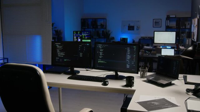 Empty cybersecurity workstation displaying programming code on multiple computer screens at night. Suitable for cyber defense commercials, software development videos, or IT presentations