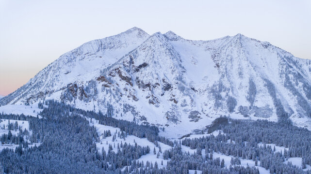 Aerial view of the snow-covered peaks of the Ruby Range and dense pine forests in the Gunnison National Forest near Crested Butte, Colorado, United States.