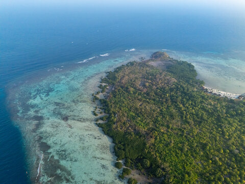 Aerial view of Karimun Jawa island featuring lush tropical vegetation, vibrant coral reefs, turquoise shallow waters, and deep blue ocean in Karimunjawa, Central Java, Indonesia.