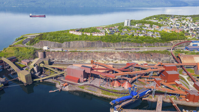 Aerial view of the industrial Narvik Harbor with its iron ore terminal, red buildings, conveyor belts, and a cargo ship docked in the fjord near the town of Narvik, Nordland, Norway.