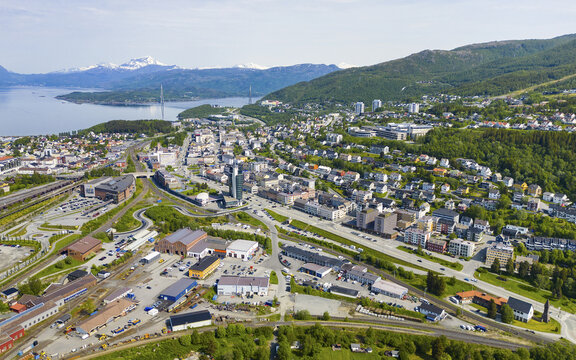 Aerial view of Narvik Harbor and the town with residential buildings, industrial areas, and railway infrastructure, set against mountains and the fjord in Narvik, Nordland, Norway.