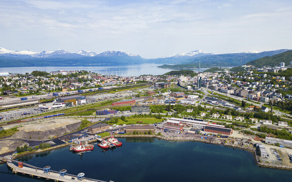 Aerial view of Narvik Harbor featuring industrial facilities, railway tracks, and urban buildings set against a backdrop of snow-capped mountains in Narvik, Nordland, Norway.