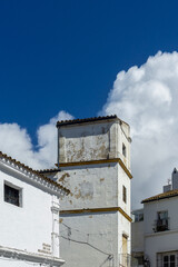 Historic white tower and traditional buildings creating a charming architectural scene under a bright blue sky with fluffy clouds, representing Spanish heritage © photoopus