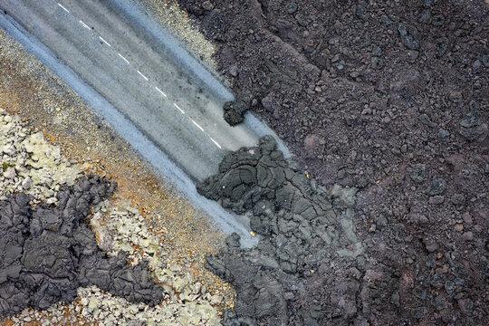 Aerial view of lava flow from Sundhnukur Volcano covering a paved road with hardened volcanic rock and dark basaltic textures in Grindavik, Grindavikurbaer, Iceland.