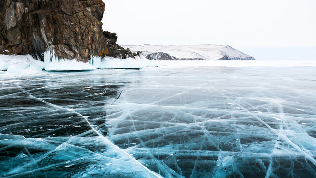 Blue transparent cracked ice and rocks on Baikal lake, Siberia, Russia. Beautiful winter landscape